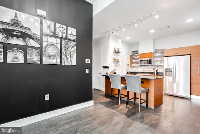 kitchen featuring a breakfast bar area, a center island, appliances with stainless steel finishes, dark hardwood / wood-style flooring, and decorative backsplash