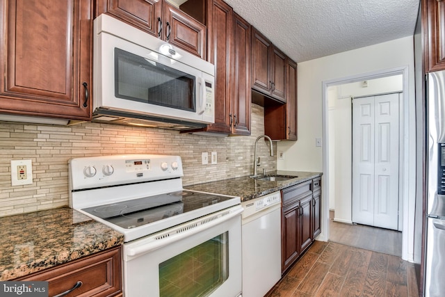 kitchen with white appliances, dark stone countertops, dark wood finished floors, a sink, and a textured ceiling