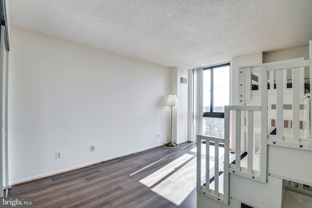 bedroom with visible vents, dark wood-type flooring, a textured ceiling, a wall of windows, and baseboards