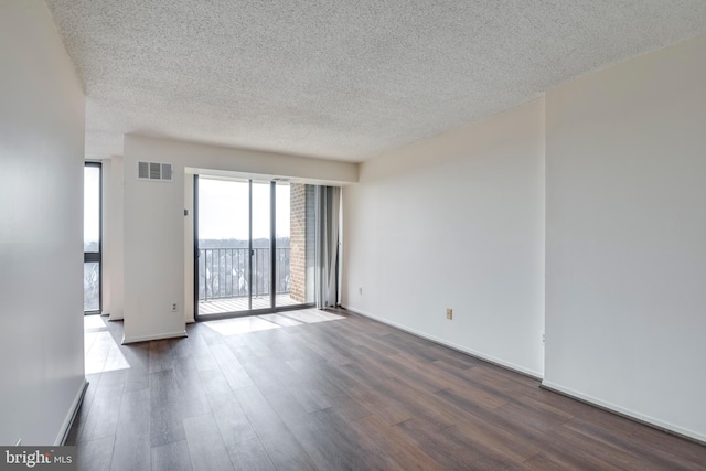 empty room featuring dark wood-style floors, visible vents, a textured ceiling, and baseboards