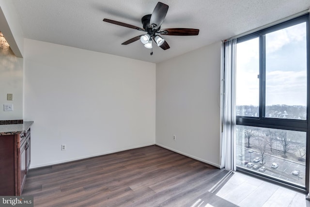 unfurnished living room with baseboards, ceiling fan, a wall of windows, wood finished floors, and a textured ceiling