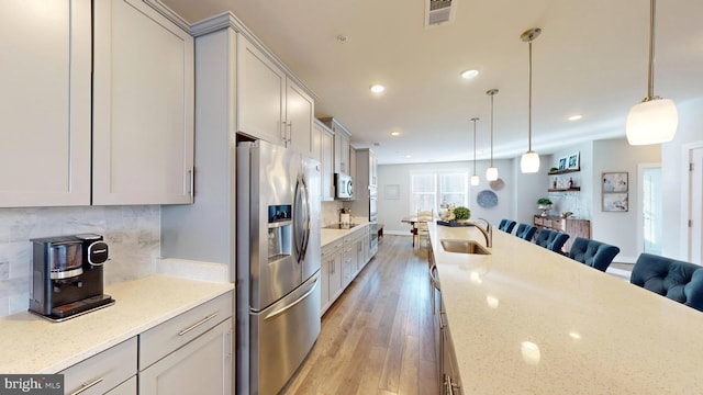 kitchen with stainless steel appliances, sink, light stone counters, and decorative light fixtures