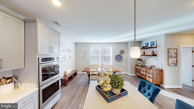 kitchen featuring double oven, white cabinets, hanging light fixtures, light stone counters, and light hardwood / wood-style floors