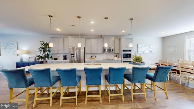 kitchen with a breakfast bar, stainless steel appliances, decorative light fixtures, and gray cabinets