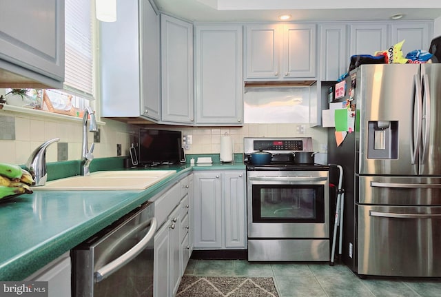 kitchen with sink, tasteful backsplash, white cabinetry, dark tile patterned flooring, and stainless steel appliances