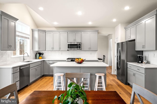 kitchen featuring sink, gray cabinets, appliances with stainless steel finishes, a center island, and a kitchen bar