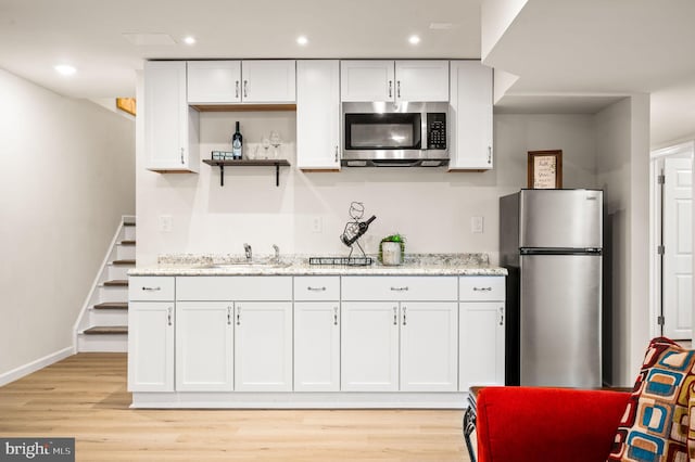 kitchen featuring white cabinetry, sink, light stone counters, stainless steel appliances, and light wood-type flooring