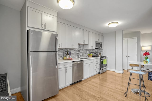 kitchen with appliances with stainless steel finishes, white cabinetry, sink, backsplash, and light wood-type flooring