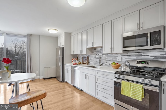 kitchen featuring sink, tasteful backsplash, light wood-type flooring, appliances with stainless steel finishes, and white cabinets