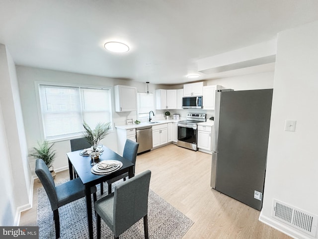 kitchen featuring sink, light hardwood / wood-style flooring, white cabinetry, hanging light fixtures, and stainless steel appliances