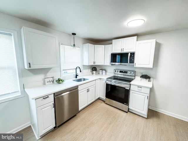 kitchen with pendant lighting, white cabinetry, sink, light hardwood / wood-style floors, and stainless steel appliances