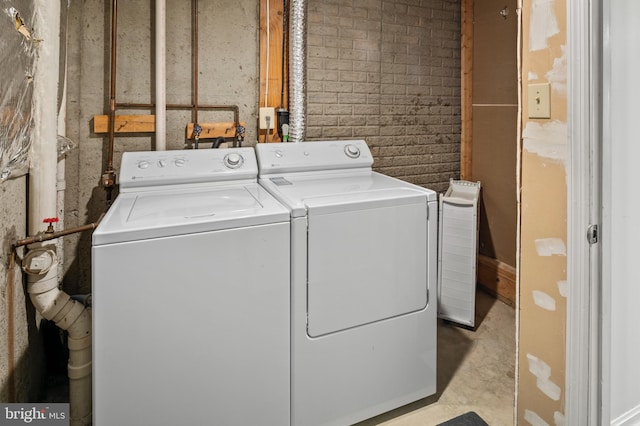 laundry area featuring brick wall and washer and clothes dryer