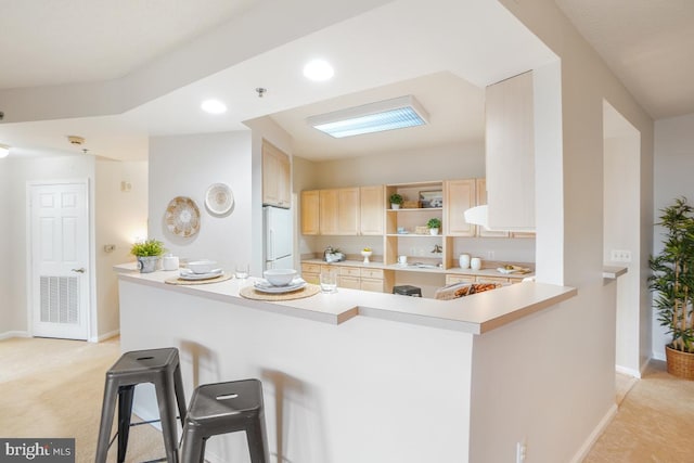 kitchen featuring a peninsula, a kitchen breakfast bar, light countertops, and freestanding refrigerator