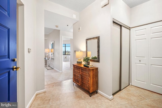 hallway with baseboards, a textured ceiling, and light tile patterned flooring