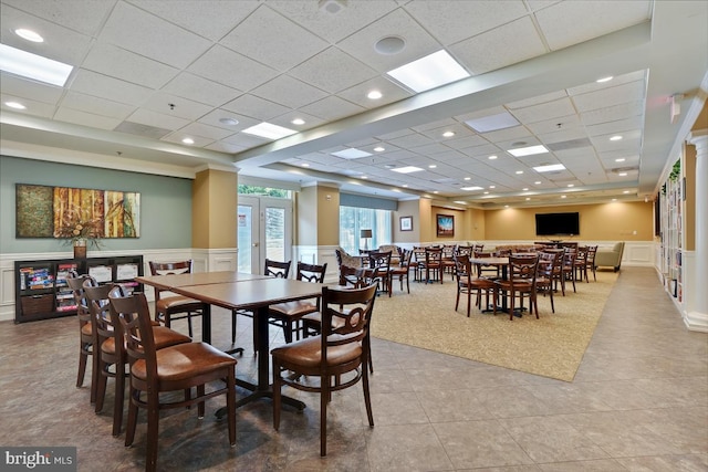 dining area with a drop ceiling, a wainscoted wall, french doors, a decorative wall, and light tile patterned flooring