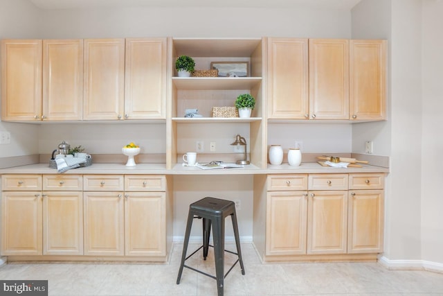 kitchen with light countertops, light brown cabinetry, a kitchen bar, and baseboards