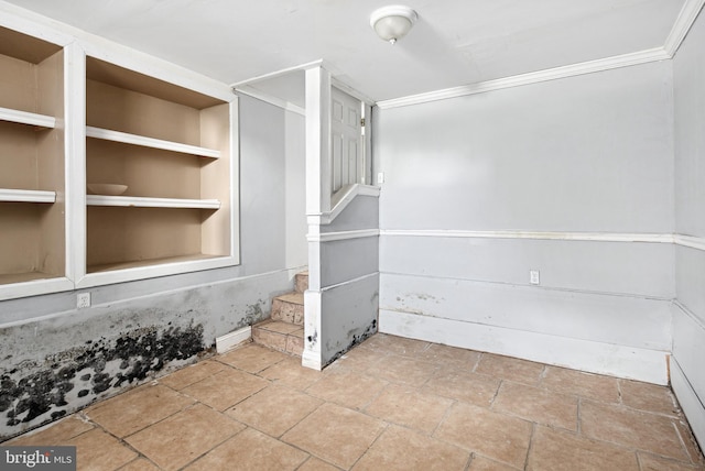 unfurnished room featuring built in shelves and crown molding