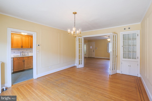 unfurnished dining area featuring french doors, crown molding, sink, and light wood-type flooring