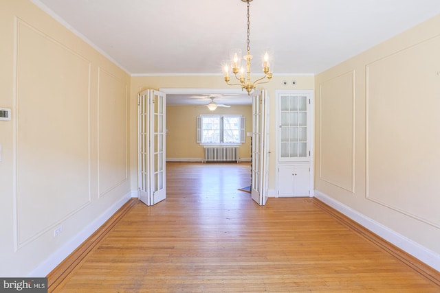 unfurnished dining area with radiator, crown molding, ceiling fan with notable chandelier, and light wood-type flooring