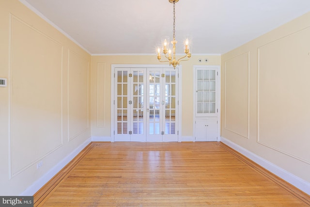 unfurnished dining area with ornamental molding, an inviting chandelier, light wood-type flooring, and french doors