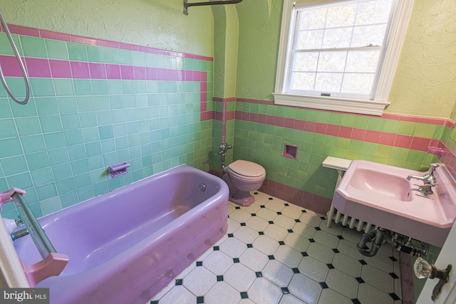 bathroom with toilet, sink, and tile walls