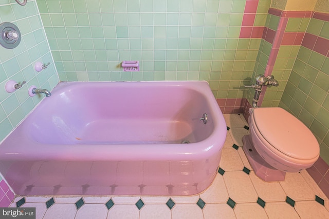 bathroom with a tub to relax in, toilet, tile patterned flooring, and tile walls