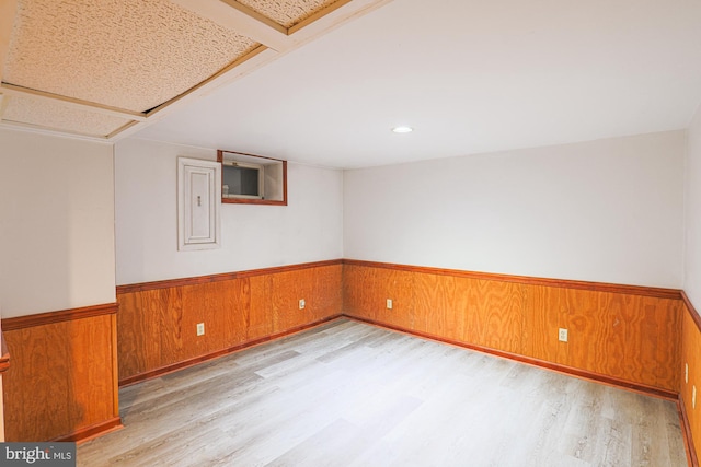 basement featuring wooden walls, electric panel, and light hardwood / wood-style floors