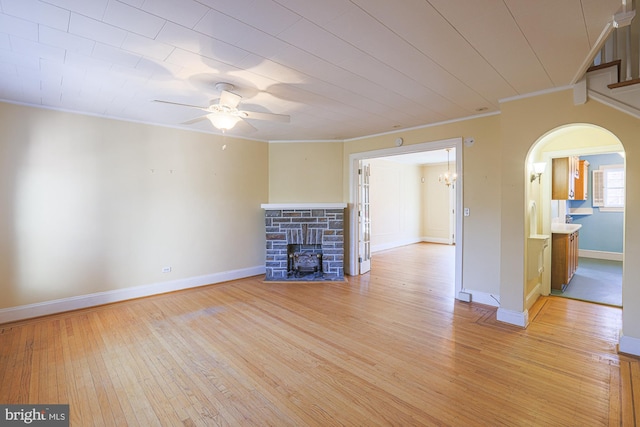 unfurnished living room featuring crown molding, ceiling fan, a stone fireplace, and light wood-type flooring