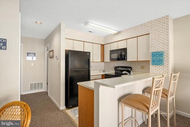 kitchen featuring light carpet, cream cabinetry, black appliances, and kitchen peninsula