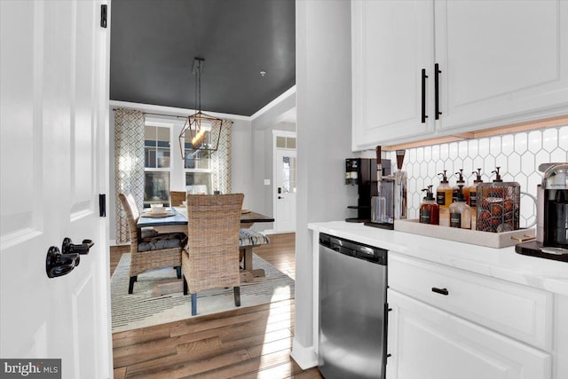 kitchen featuring decorative light fixtures, stainless steel dishwasher, white cabinets, hardwood / wood-style floors, and backsplash