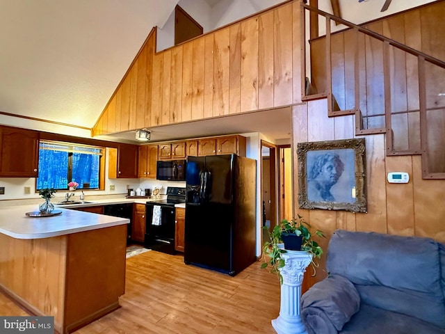 kitchen with high vaulted ceiling, black appliances, sink, kitchen peninsula, and light wood-type flooring