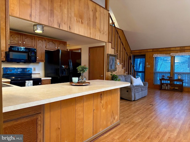 kitchen with high vaulted ceiling, light wood-type flooring, wooden walls, kitchen peninsula, and black appliances