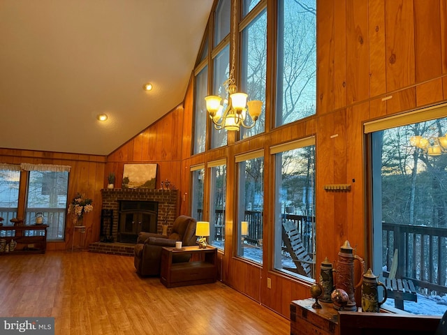 living room with light hardwood / wood-style flooring, high vaulted ceiling, a notable chandelier, a brick fireplace, and wood walls