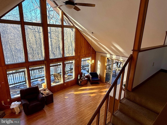 living room featuring hardwood / wood-style flooring, high vaulted ceiling, ceiling fan, and wood walls