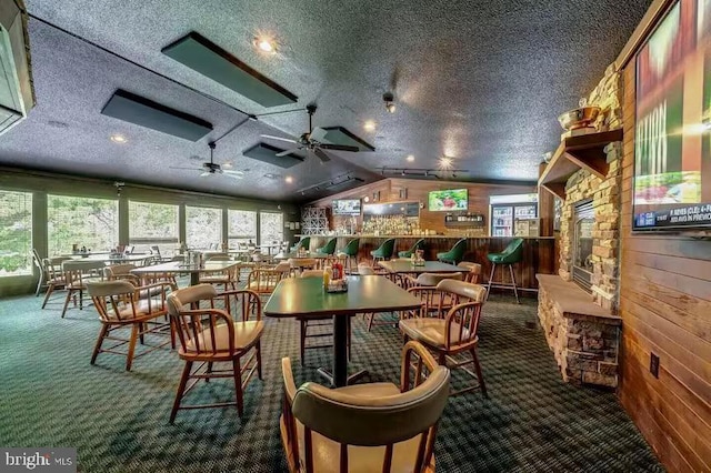 dining space featuring wood walls, dark colored carpet, vaulted ceiling, a textured ceiling, and ceiling fan