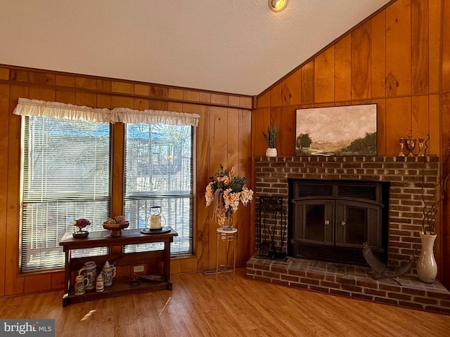 living area with a fireplace, vaulted ceiling, light hardwood / wood-style floors, and wooden walls