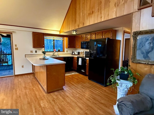 kitchen featuring high vaulted ceiling, black appliances, sink, kitchen peninsula, and light hardwood / wood-style flooring