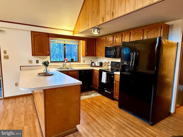 kitchen with lofted ceiling, light hardwood / wood-style flooring, kitchen peninsula, and black appliances