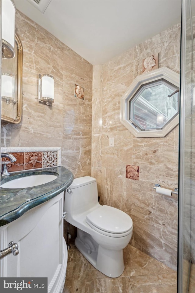 bathroom with vanity, toilet, and tile walls