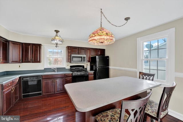 kitchen featuring sink, dark wood-type flooring, a breakfast bar area, black appliances, and decorative light fixtures