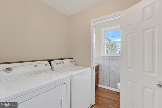 clothes washing area with washing machine and dryer, tile walls, and light hardwood / wood-style floors