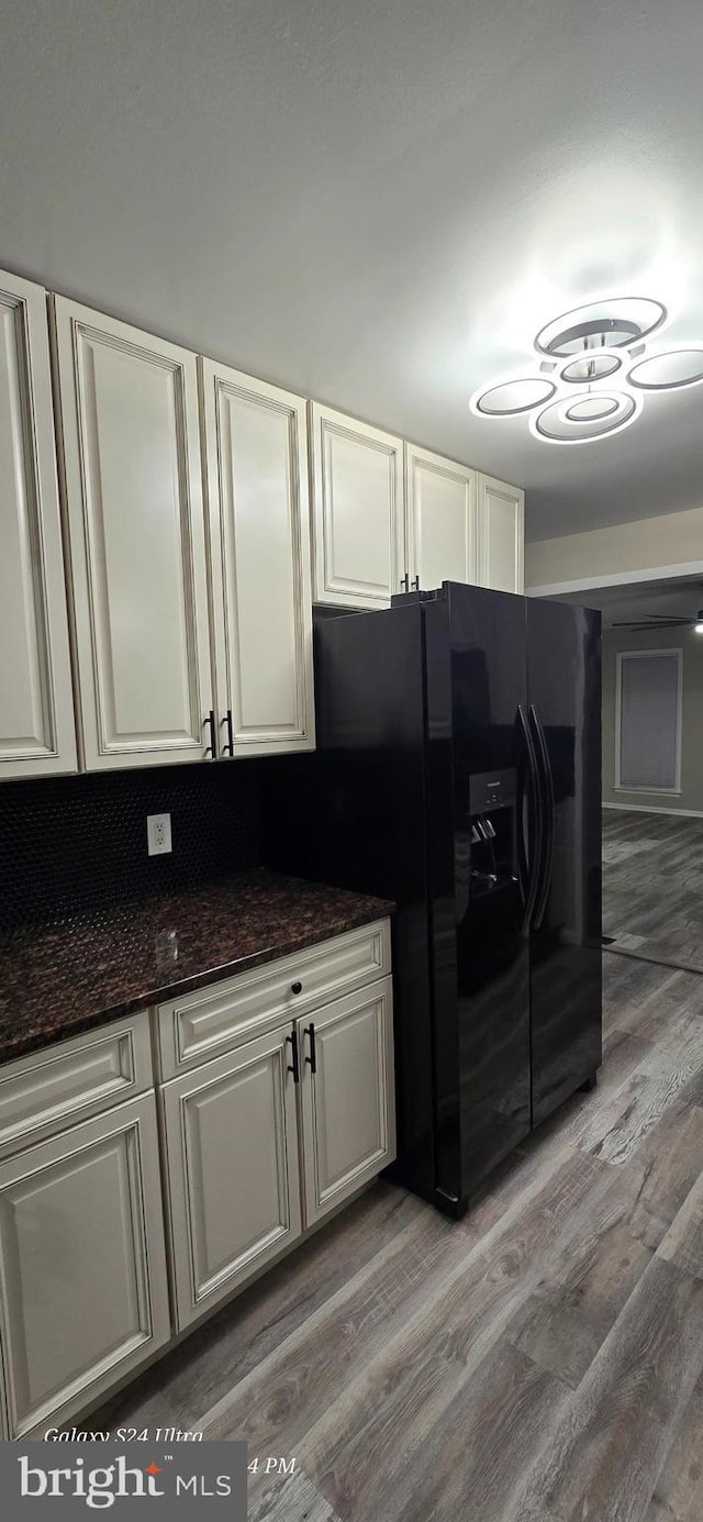 kitchen with hardwood / wood-style flooring, white cabinets, dark stone counters, and black refrigerator with ice dispenser