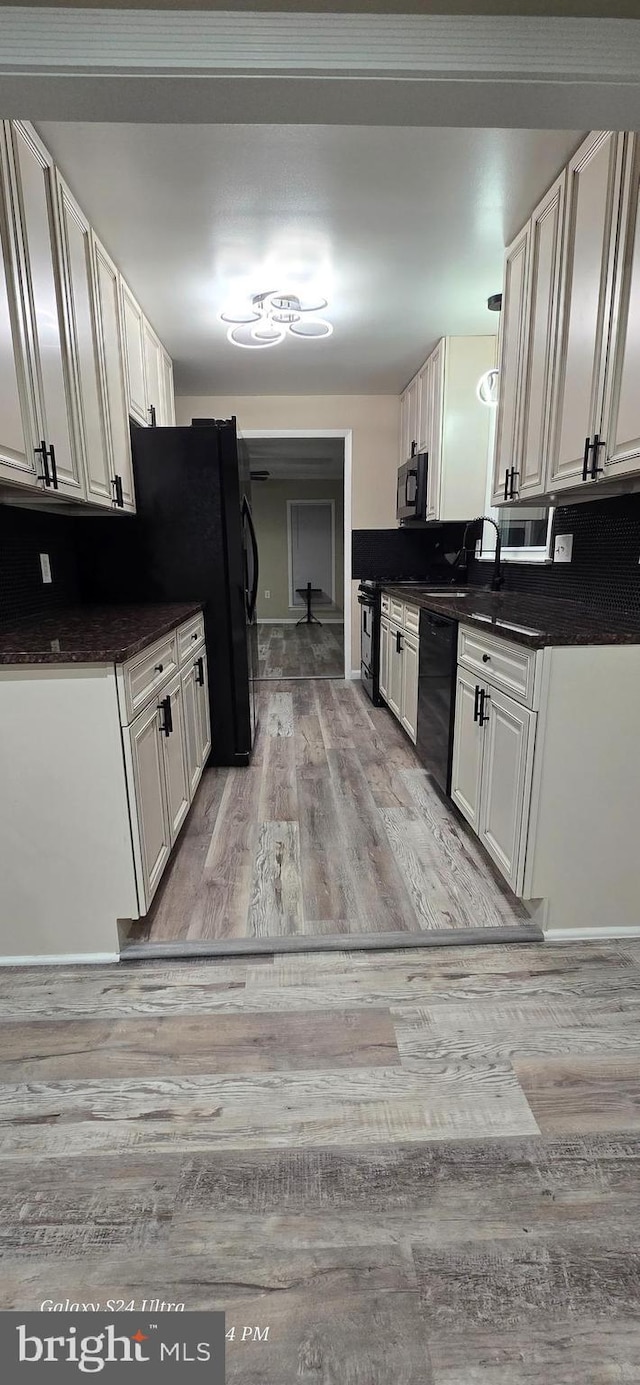 kitchen with sink, black appliances, light hardwood / wood-style floors, and white cabinets