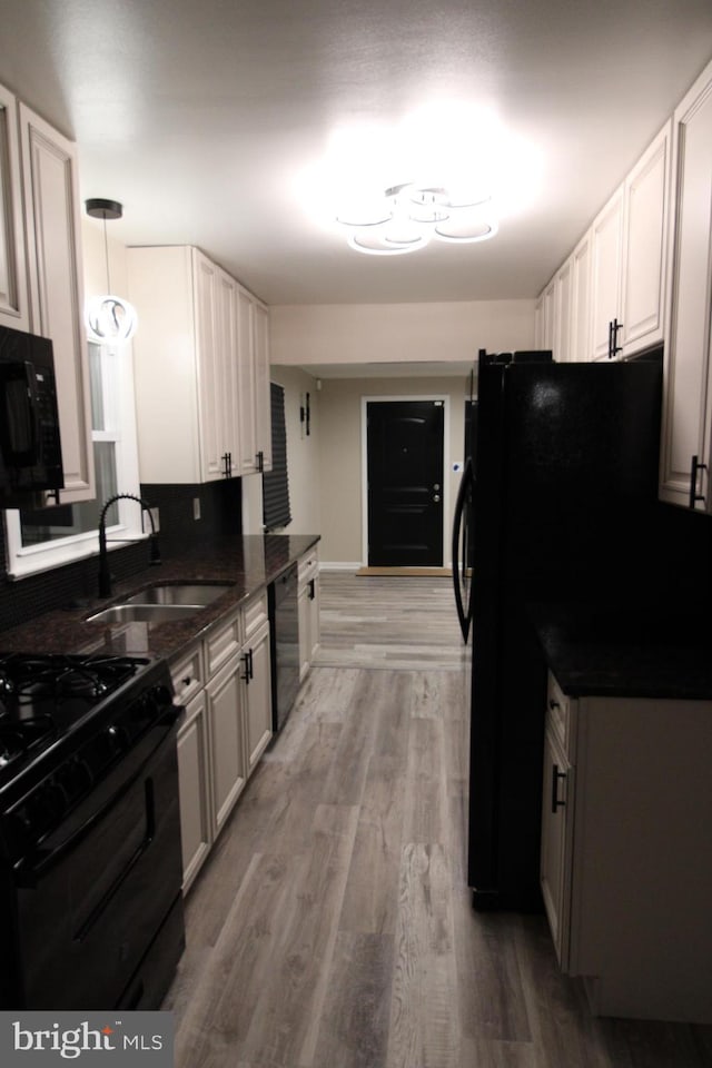 kitchen with white cabinetry, sink, hanging light fixtures, black appliances, and light hardwood / wood-style flooring