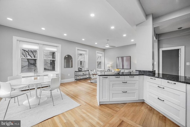 kitchen featuring ceiling fan, white cabinetry, light hardwood / wood-style floors, kitchen peninsula, and dark stone counters