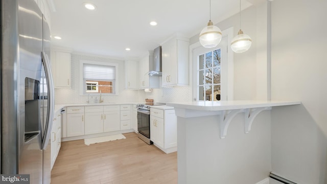 kitchen with white cabinetry, appliances with stainless steel finishes, decorative light fixtures, and wall chimney exhaust hood