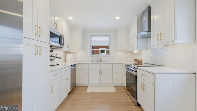 kitchen featuring appliances with stainless steel finishes, white cabinetry, sink, wall chimney exhaust hood, and light hardwood / wood-style flooring