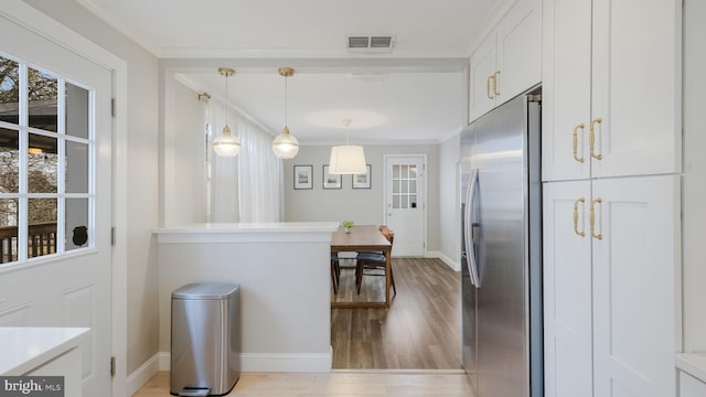 kitchen featuring stainless steel refrigerator with ice dispenser, crown molding, light wood-type flooring, pendant lighting, and white cabinets