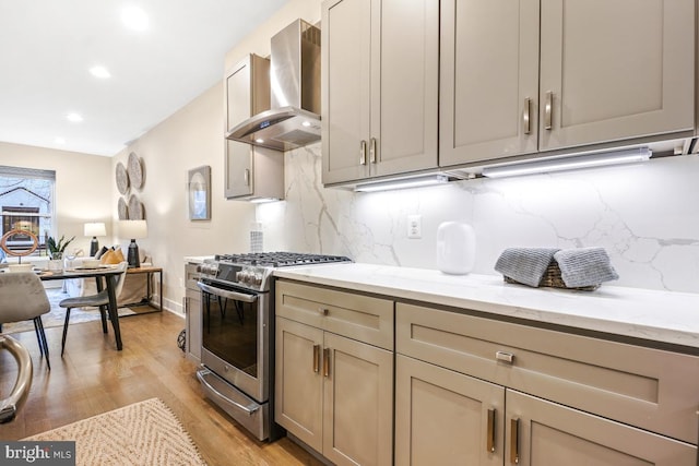 kitchen featuring wall chimney range hood, light hardwood / wood-style flooring, light stone counters, tasteful backsplash, and gas stove