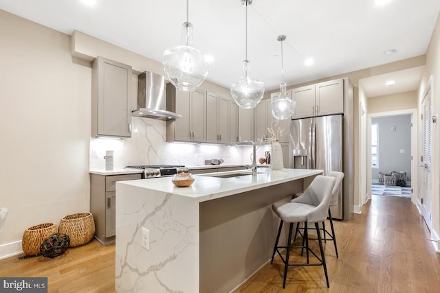 kitchen featuring sink, gray cabinetry, stainless steel fridge, a kitchen island with sink, and wall chimney exhaust hood